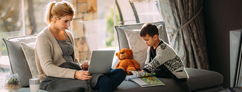Mother using laptop sitting next to child