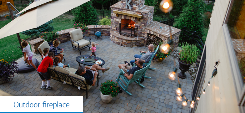 A family in their backyard in front of a fireplace. Caption reads, “Outdoor fireplace.”