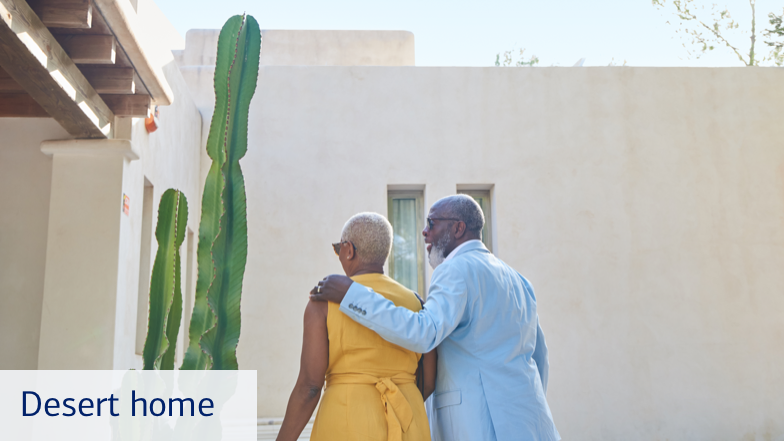A middle-aged couple, shown from the back, standing outside of their desert home, which has a tall cactus. The man has his arm around the woman. Text on the bottom left of this slide reads, “Desert Home.”