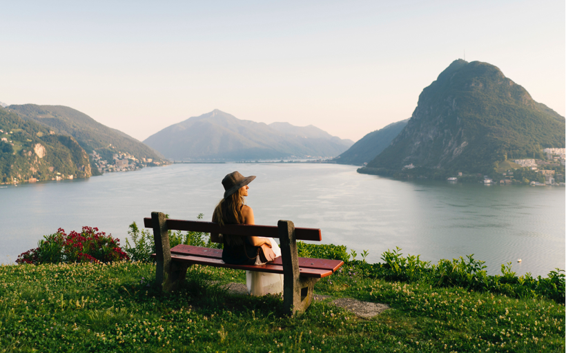 Image of a woman sitting on a bench near a lake and mountain