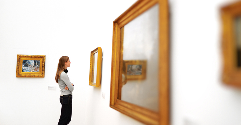 A woman studies a painting on the wall of a museum